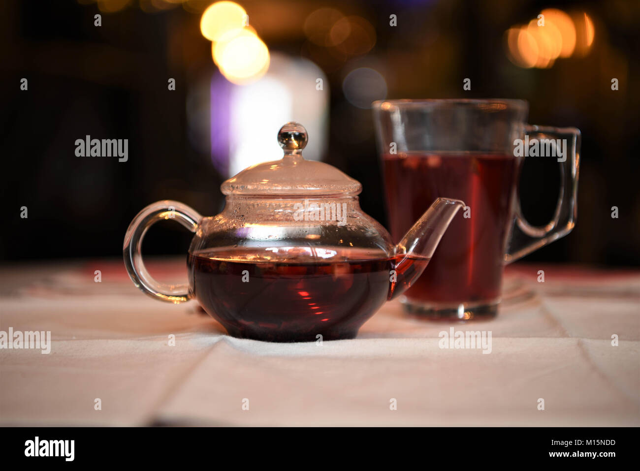 drink image of a hot fruit flavored red color tea made in a glass teapot with poured glass cup and with bokeh blurred light background and atmosphere Stock Photo