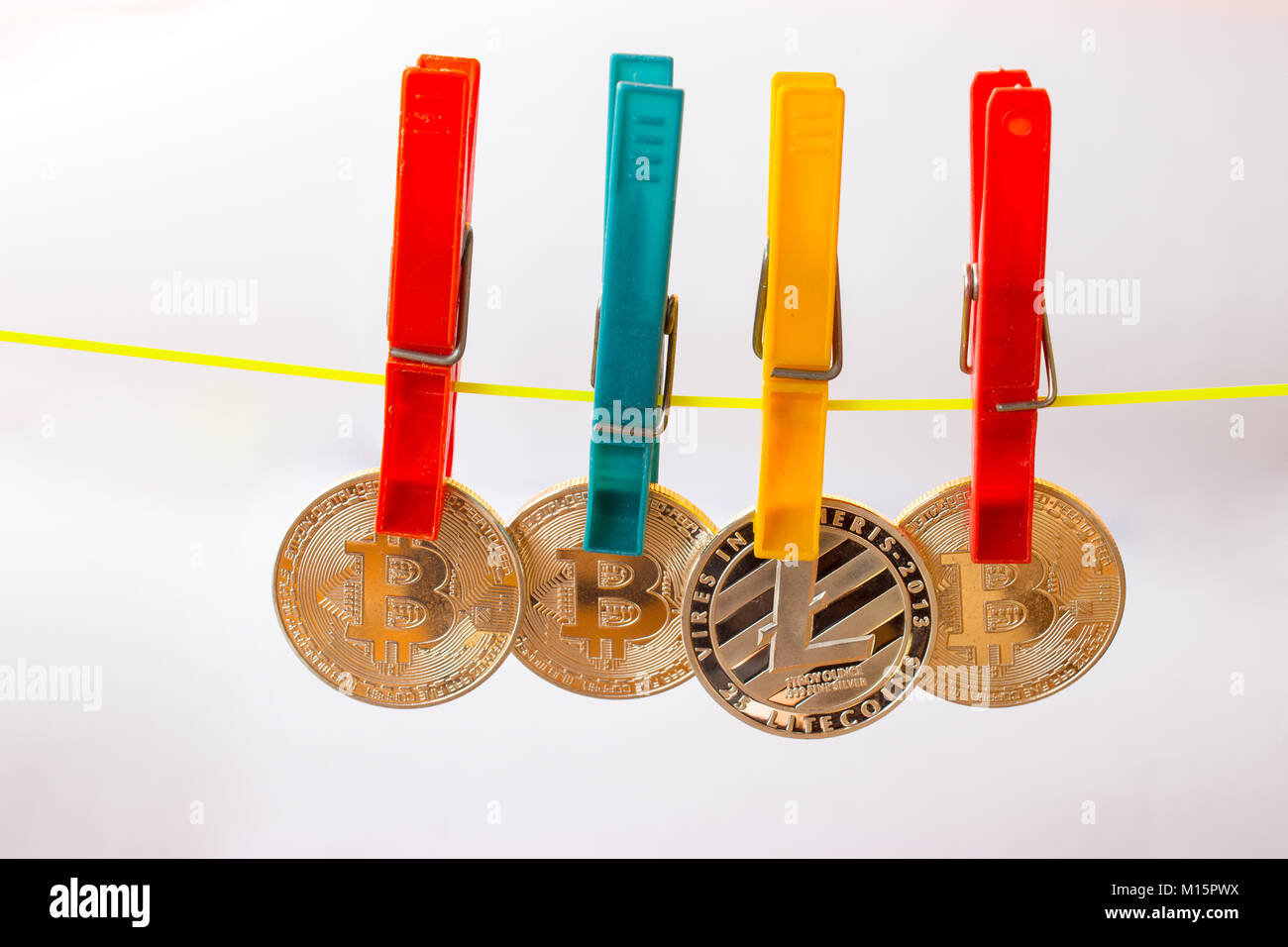 Colorful clothespins hold bitcoins and litecoin on a clothesline. The background is white. Stock Photo
