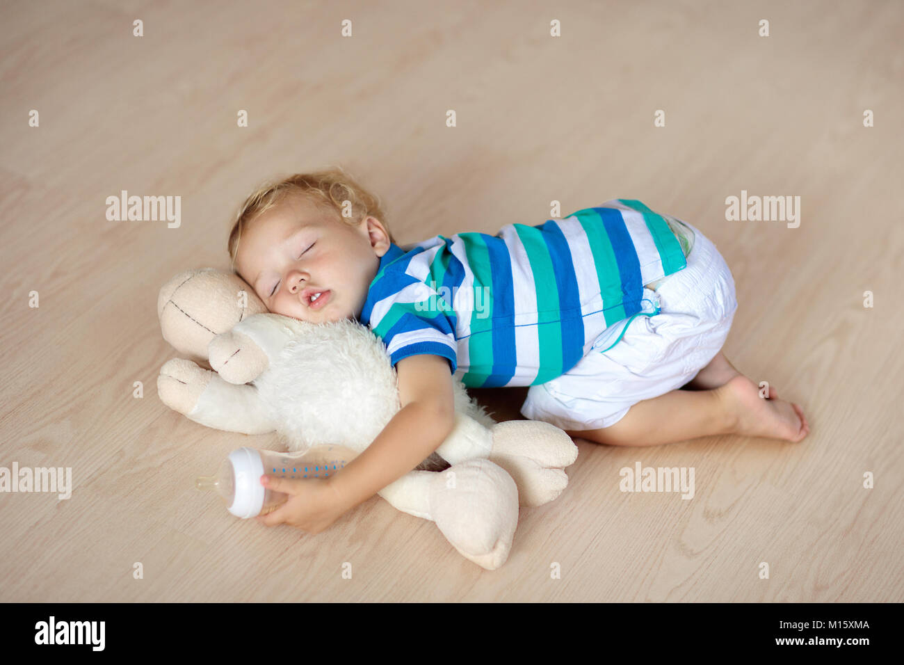 Baby sleeping on wooden floor with stuffed toy sheep and milk bottle