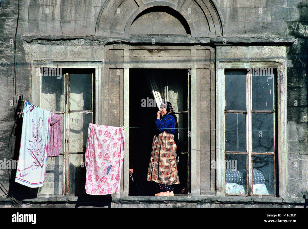 Traditional Turkish Woman Hanging Out Washing Outside Old Apartment Building in Galata District, Istanbul, Turkey Stock Photo