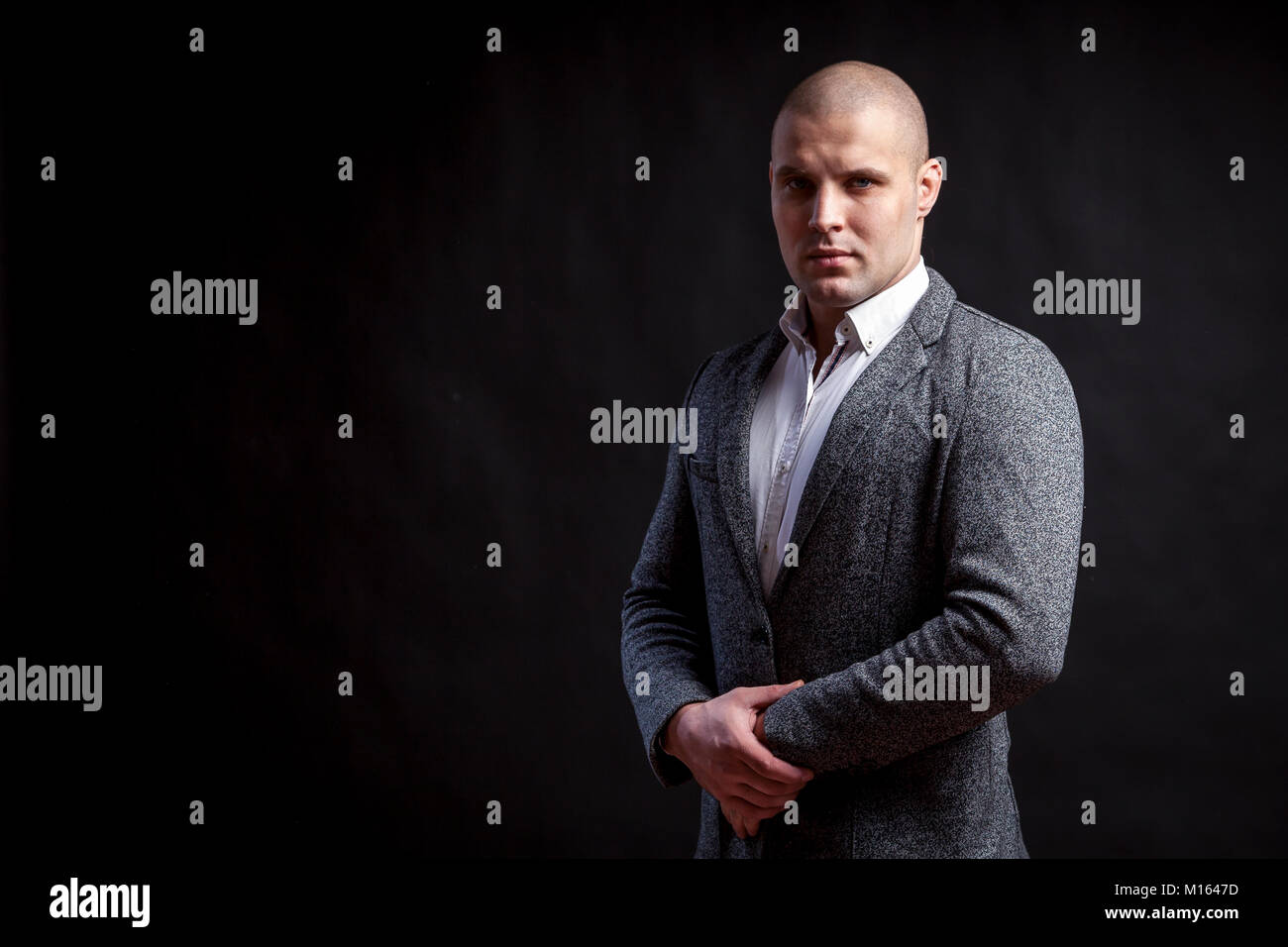 Young bald man in white shirt, gray suit confidently looks at camera and posing on black isolated background Stock Photo