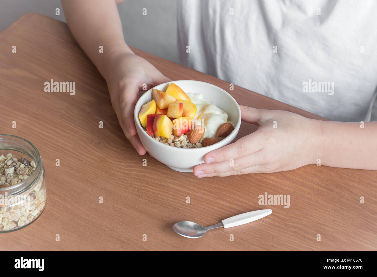 Eating healthy breakfast bowl. Oatmeal granola, yougurt, fresh nectarins inwhite bowl in female (child) hands over wooden table. Clean eating, dieting Stock Photo