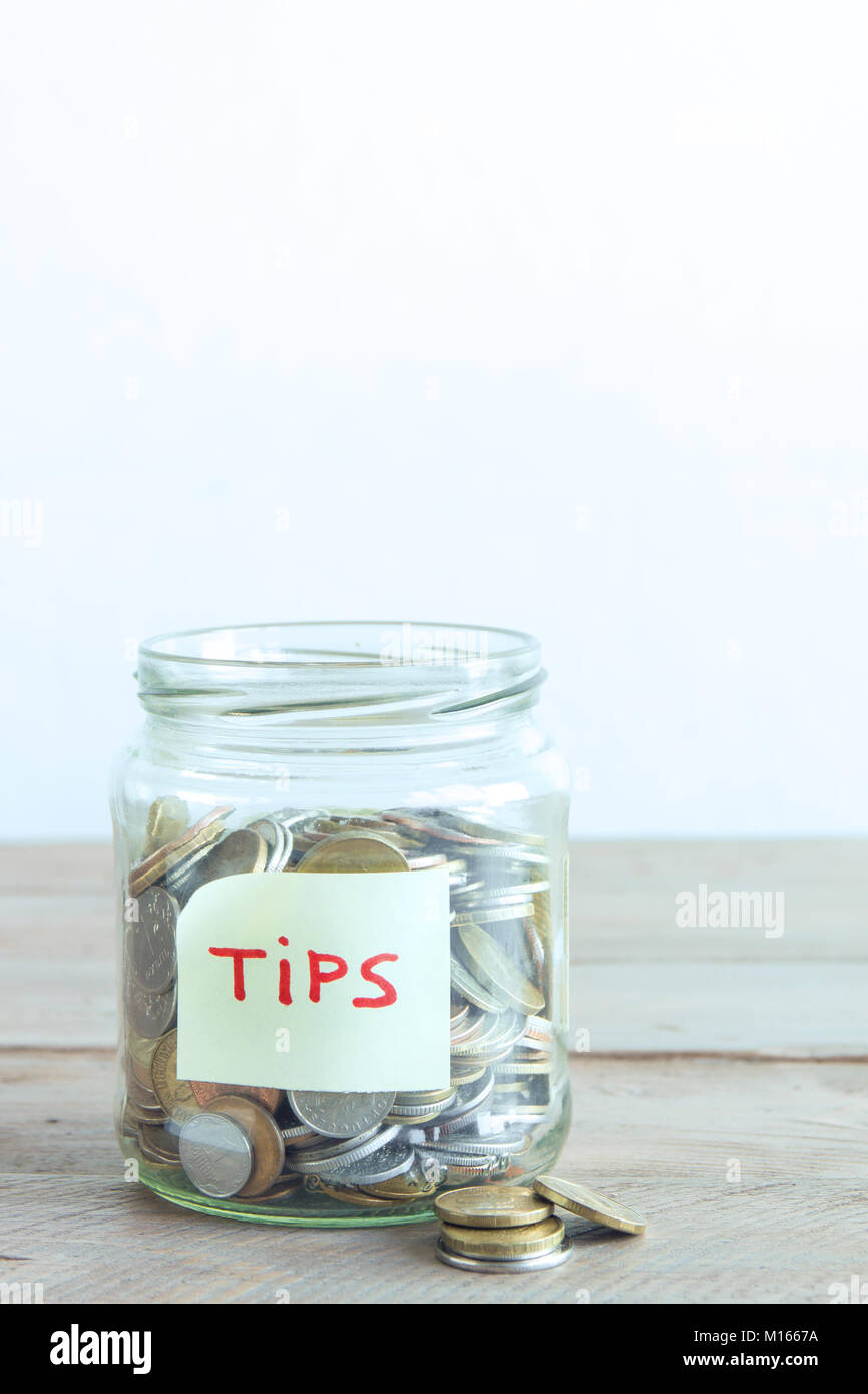 Coins in glass jar with Tips label. Money savings, tips and donation concept, copy space. Stock Photo