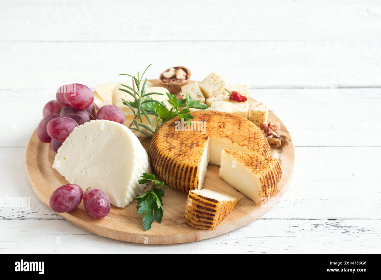 Cheese platter with assorted cheeses, grapes, nuts over white wooden