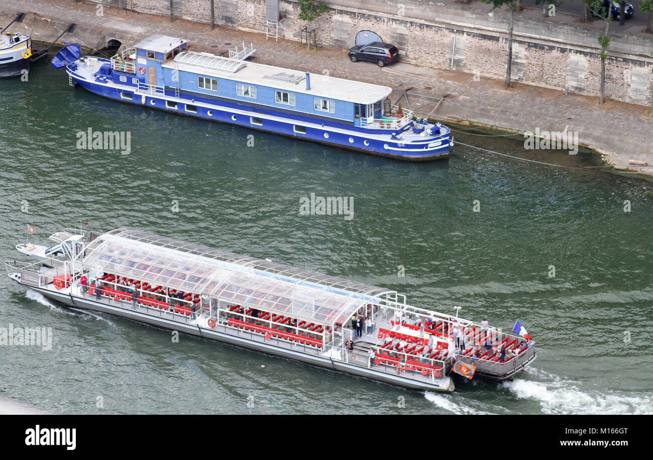 A Blue cruise boat called the Blue Shadow and a Bateaux Parisiens shuttle cruise boat with a car parked on the Seine River bank, Paris, France. Stock Photo