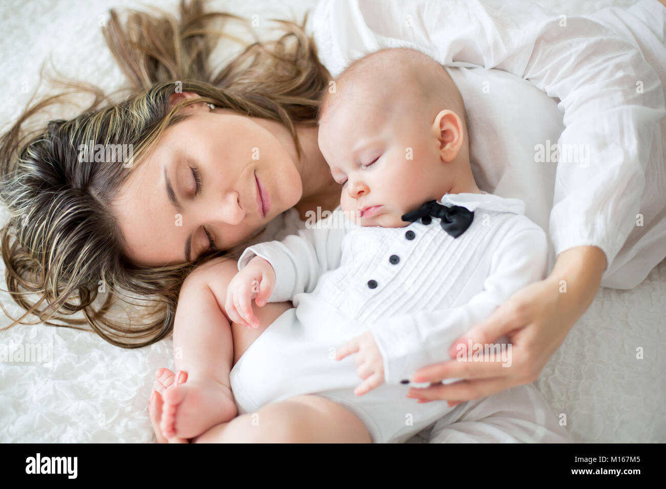 Mother and her baby son, sleeping on a big bed, soft back light ...