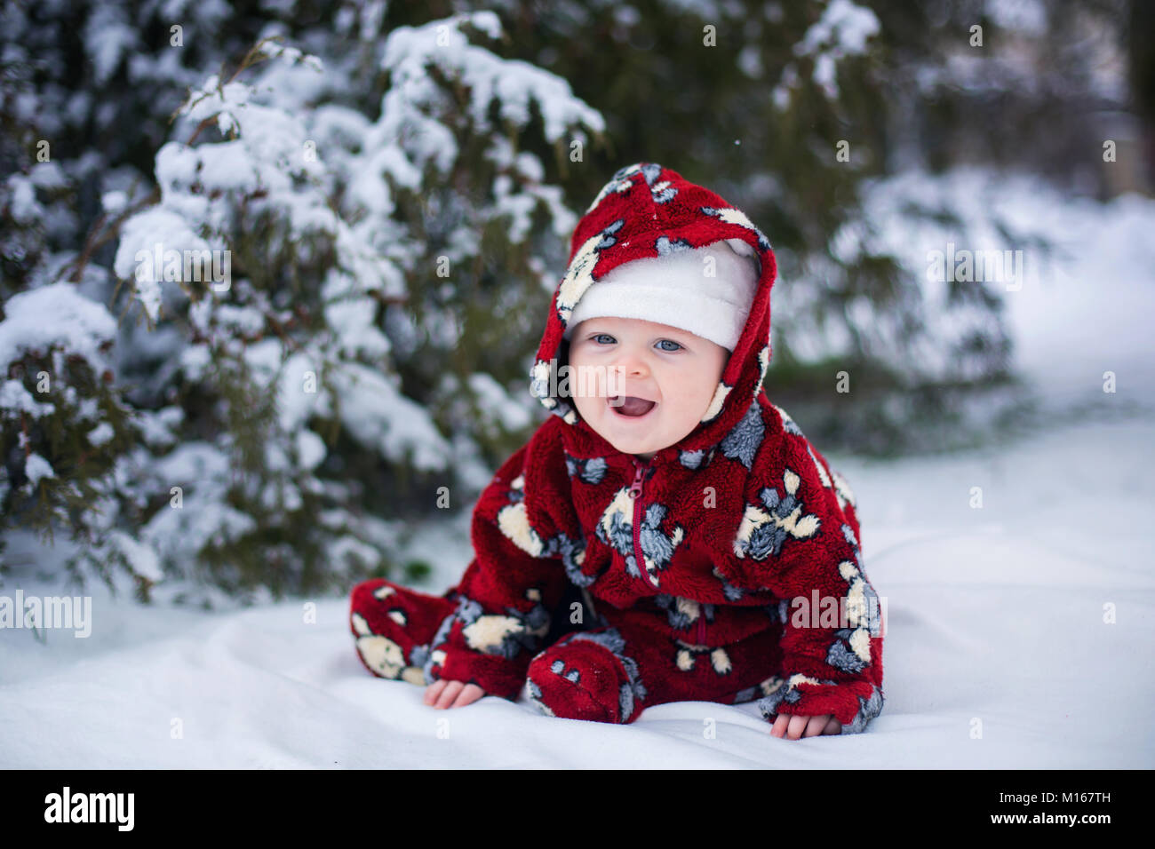 Little cute smiling baby boy, sitting outdoors in the snow next to ...