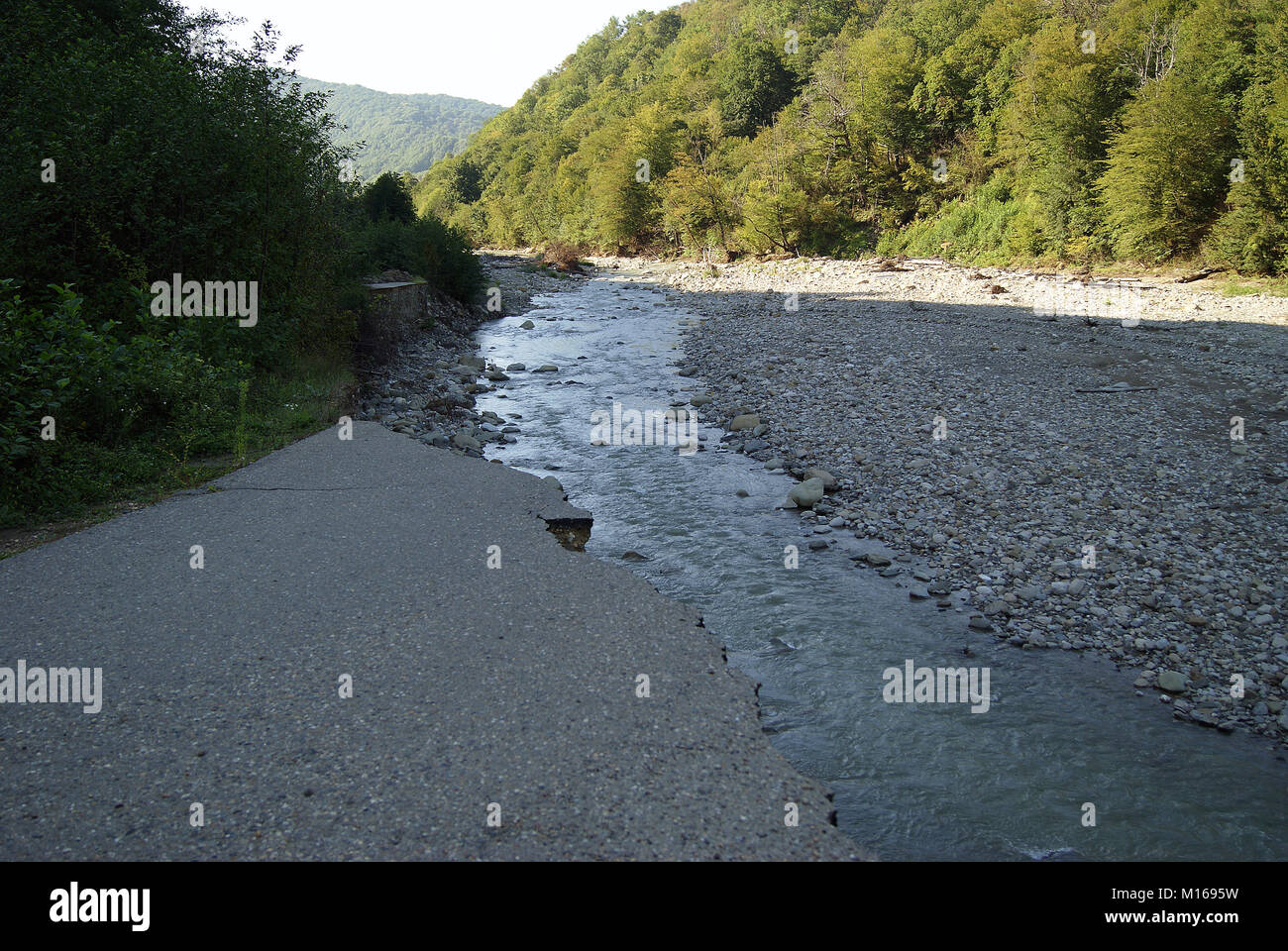 landscape overlooking the valley of a mountain river; in the foreground - an asphalt, suddenly ending in the breakage, with a torn edge: a section of  Stock Photo