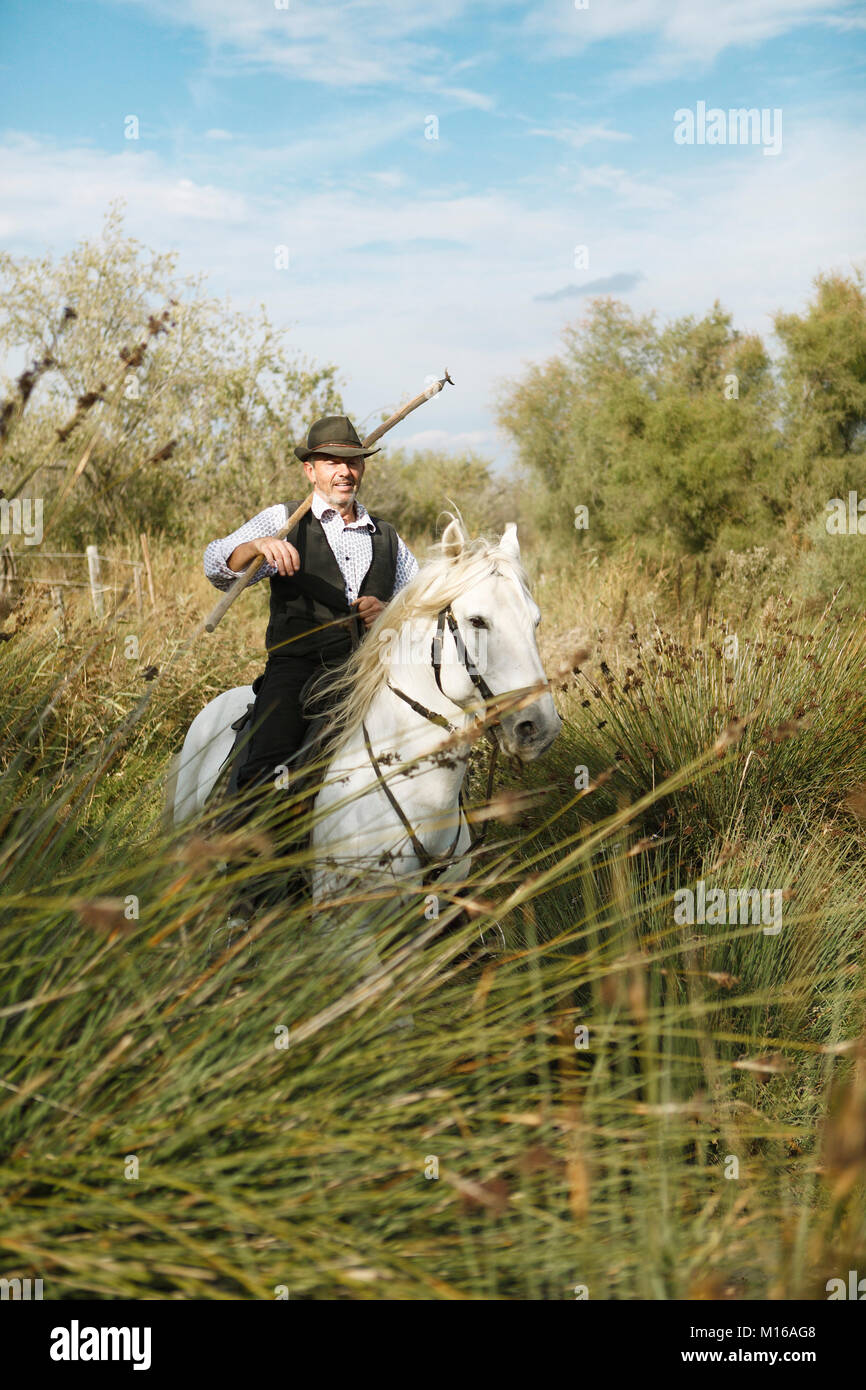 Gardian or traditional bull herder in typical working clothes galloping on a Camargue horse, Le Grau-du-Roi, Camargue, France Stock Photo
