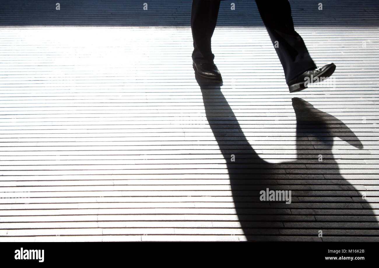 Blurry one  man's  legs silhouette and shadow on city street patterned passage walkway in black and white Stock Photo