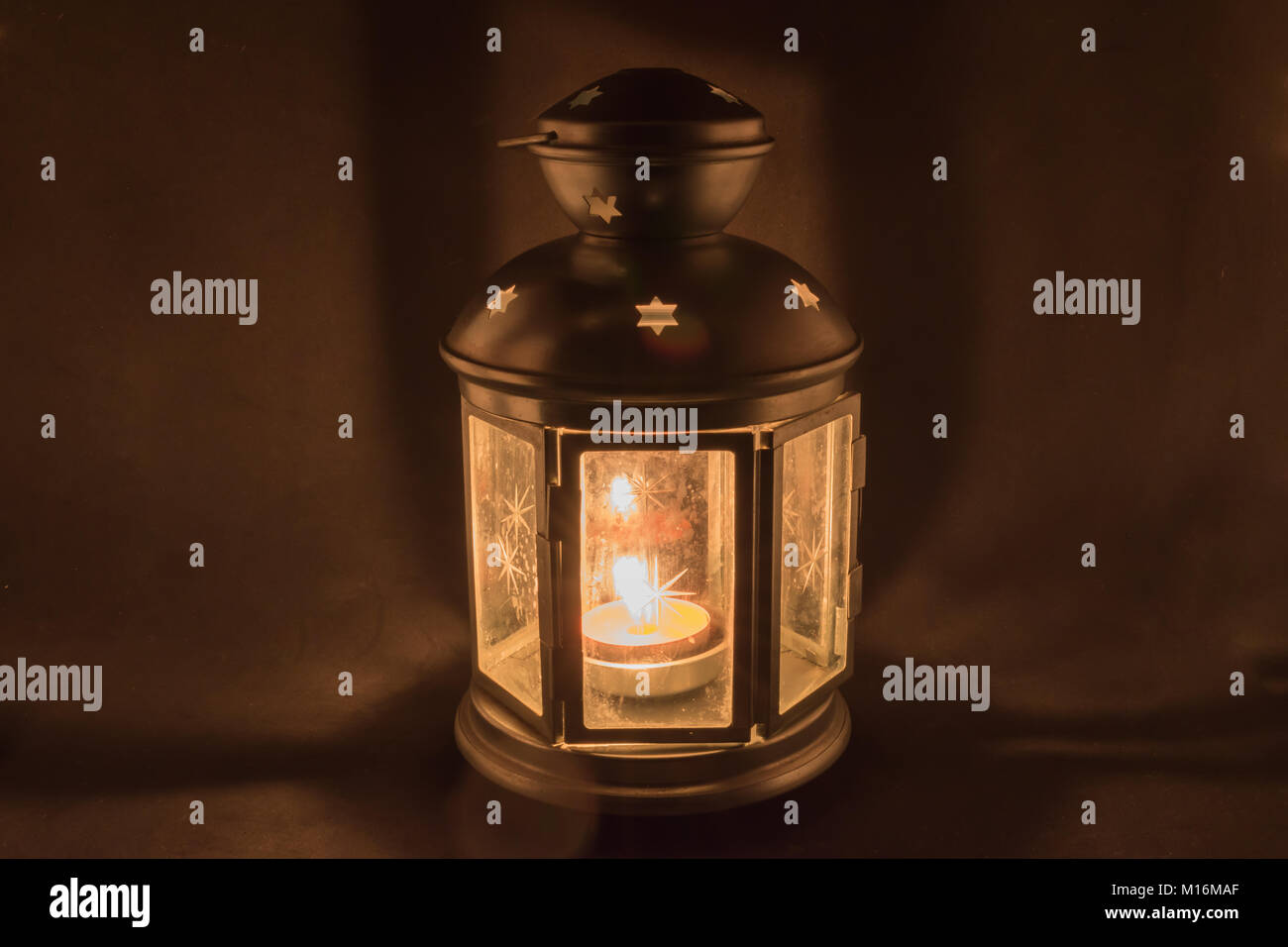 Golden lantern with a lighted candle inside on dark background with