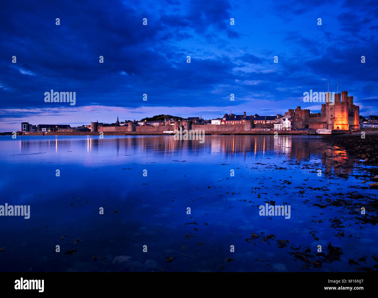 Caernarfon castle at dusk on the North Wales coast, with reflections in the sea Stock Photo