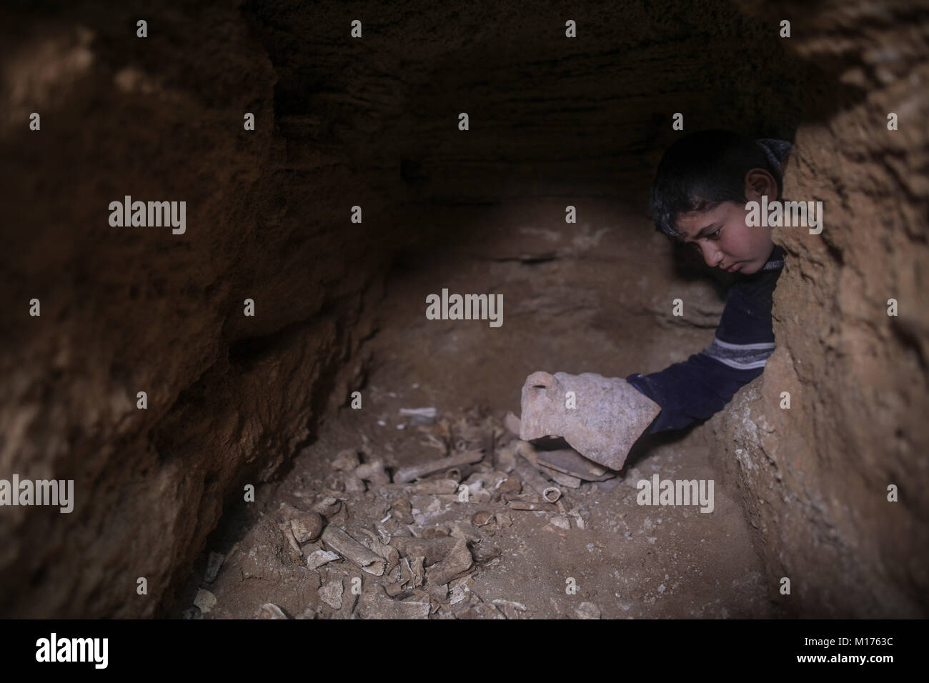 Beit Hanoun, Northern Gaza City. 27th Jan, 2018. A Palestinian boy checks potteries and bones found in a discovered tomb consisting of nine burial holes, in Beit Hanoun, Northern Gaza City, 27 January 2018. Archaeologists in Gaza say they believe the graveyard is about 2,000-year-old, dating back to the Roman era, where Gaza was part of the far-flung Roman Empire. Further tests are to be carried out to determine THE exact age. Credit: Wissam Nassar/dpa/Alamy Live News Stock Photo