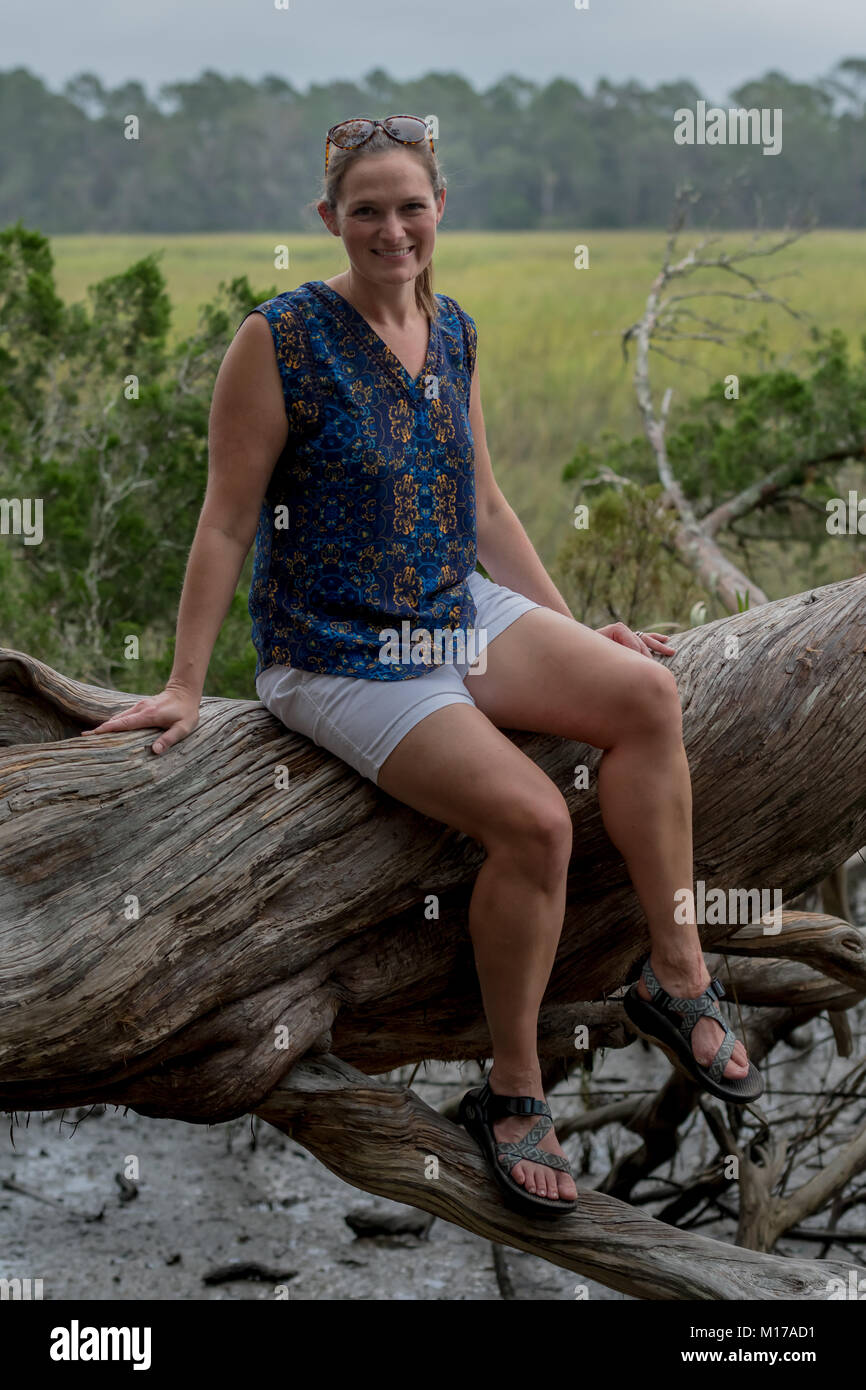 Woman Sits on Large Tree trunk in front of grassy marsh Stock Photo