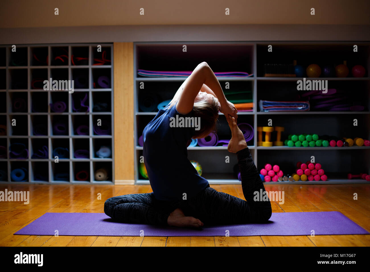 Beautiful young woman working out in gym interior, doing yoga exercise on blue mat, stretching, Stock Photo