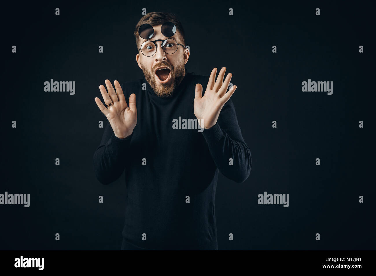 Young bearded man in black looking with surprise at camera wearing ...