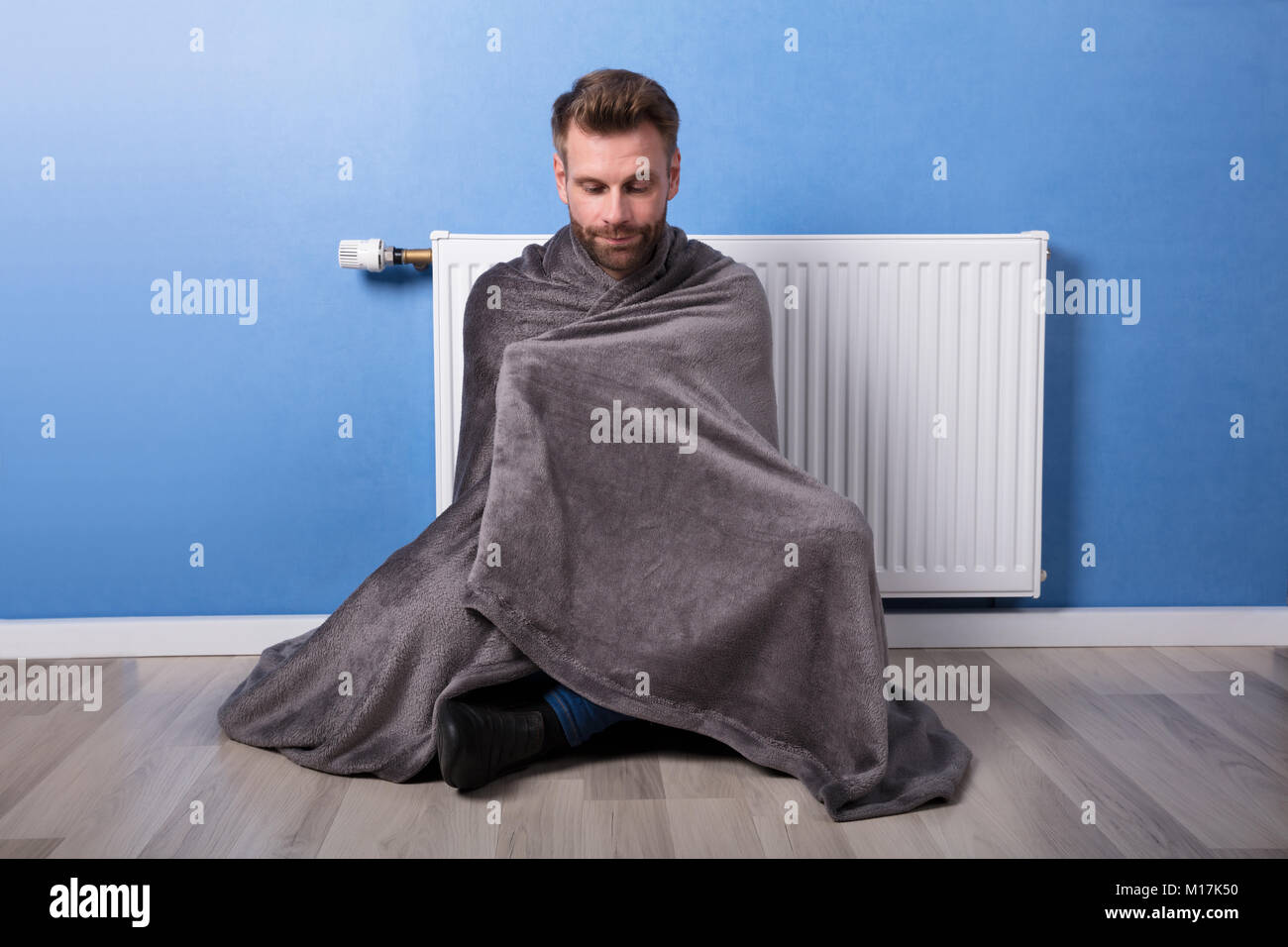 Young Man Wrapped In Blanket Sitting In Front Of Heater At Home Stock