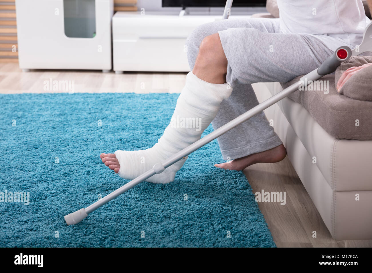 Young Man With Broken Leg Using Crutches To Get Up From Sofa Stock