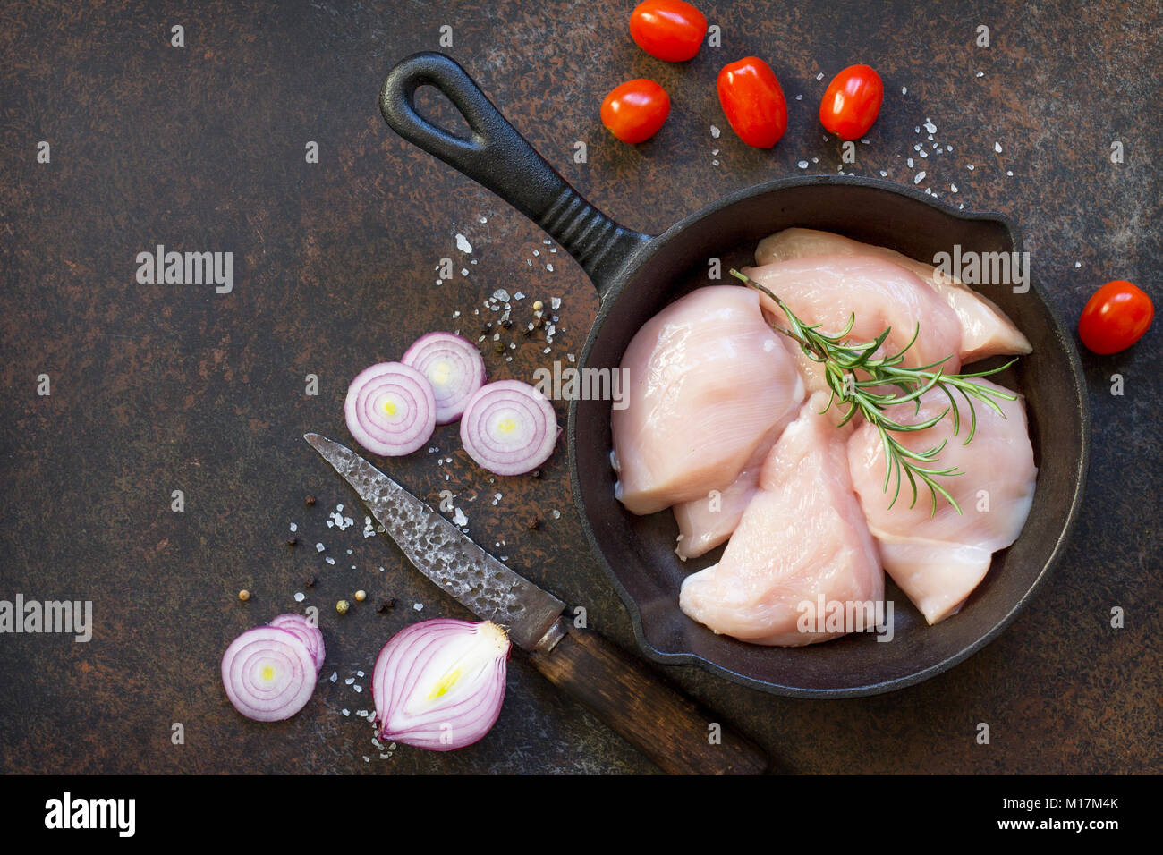 Fresh meat. Raw chicken fillet on a cast-iron frying pan, spices and fresh rosemary on the kitchen table. Top view with a copy. Stock Photo