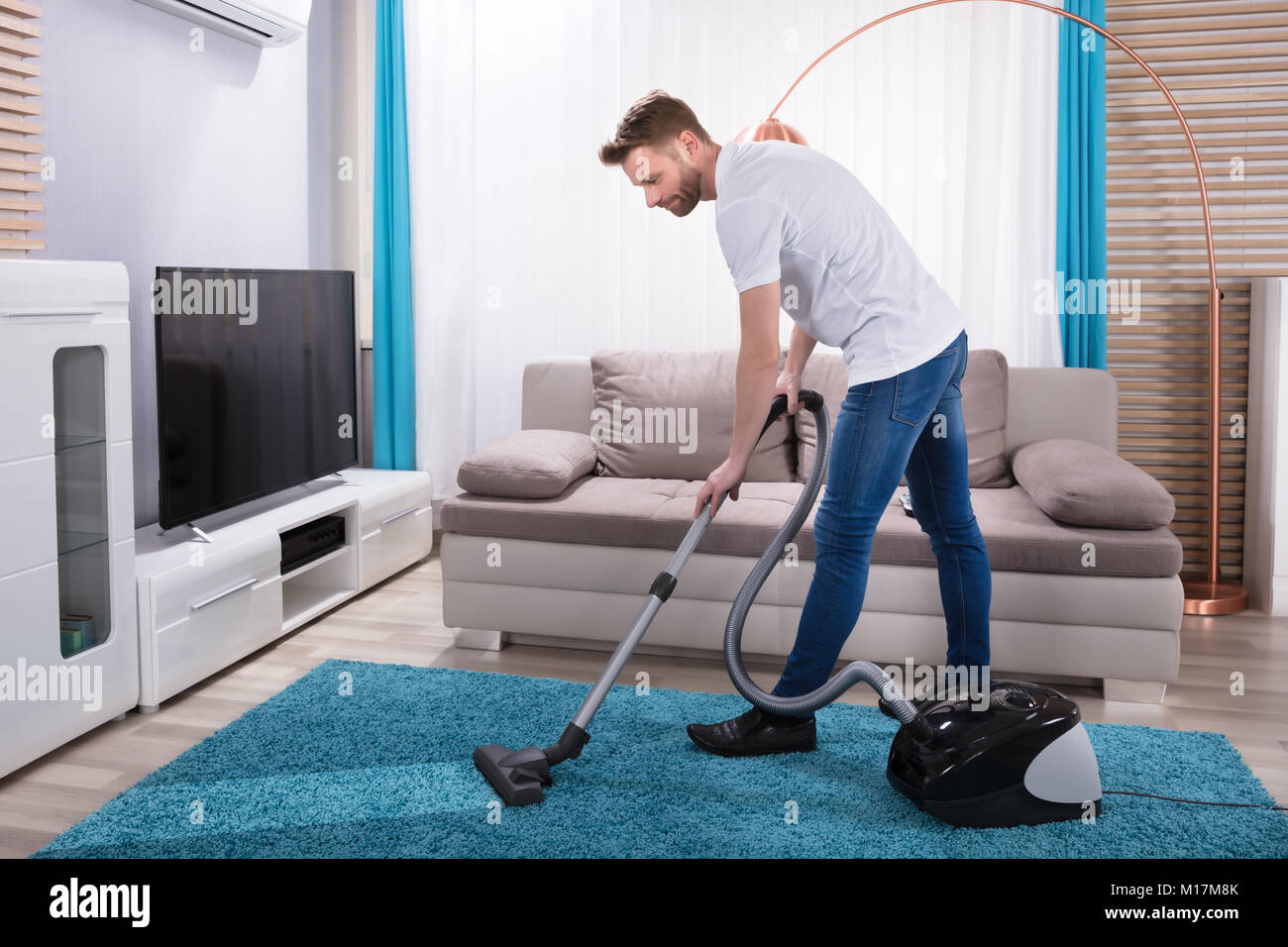 Young Man Cleaning Blue Carpet With Vacuum Cleaner At Home Stock Photo