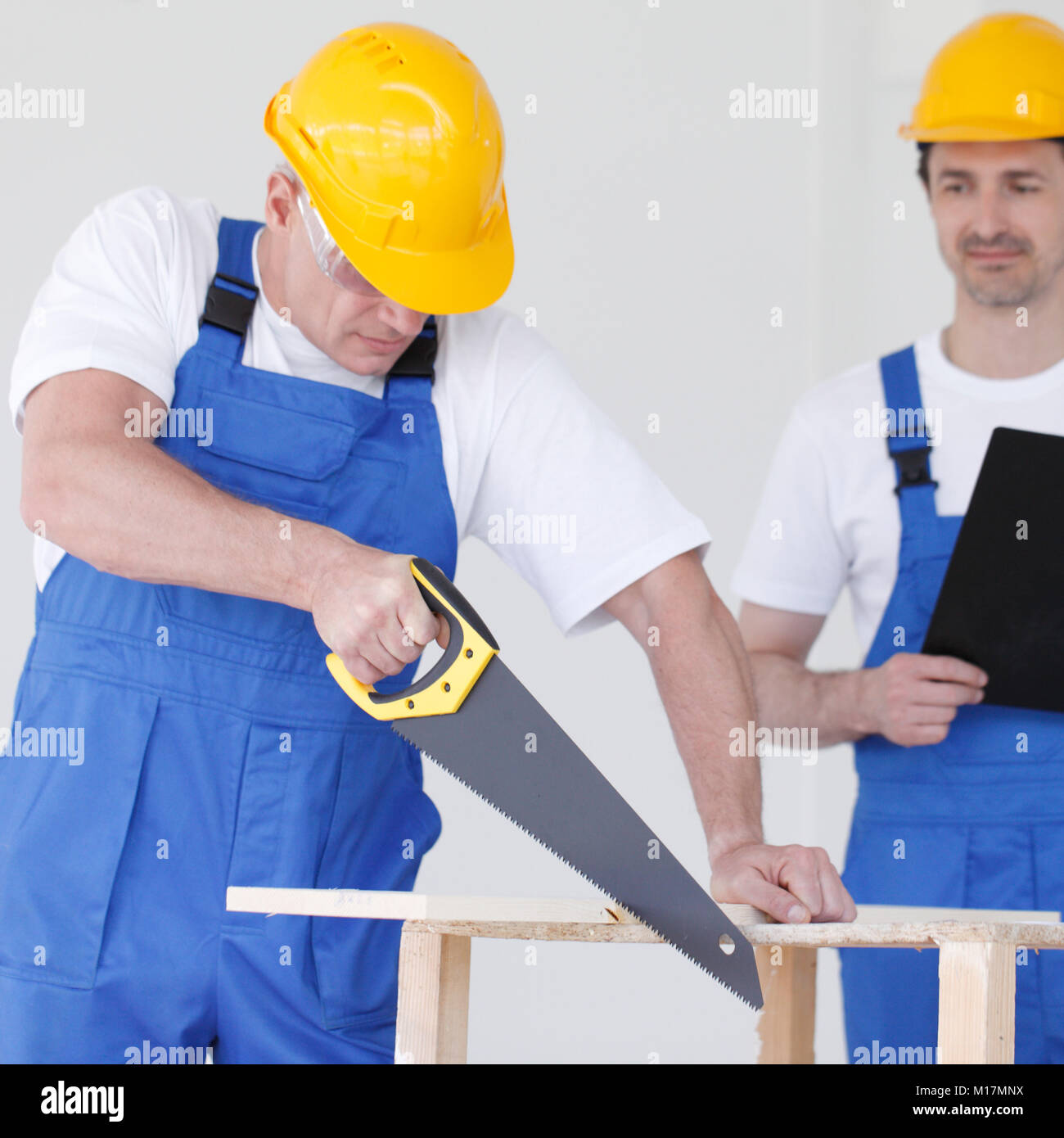 Worker works with handsaw, foreman on background Stock Photo