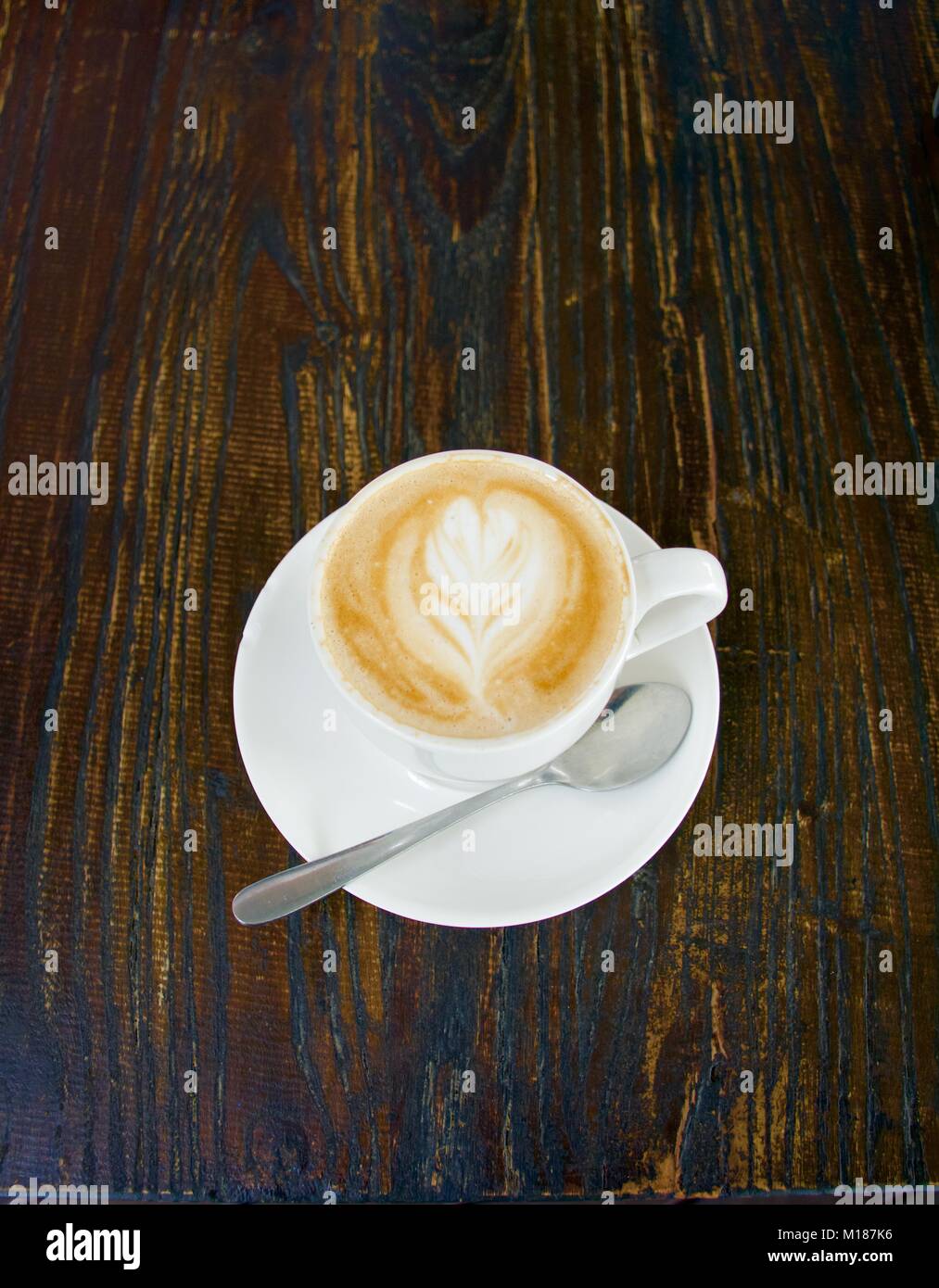 Flat White coffee with pattern in foam with spoon on a dark timber background Stock Photo