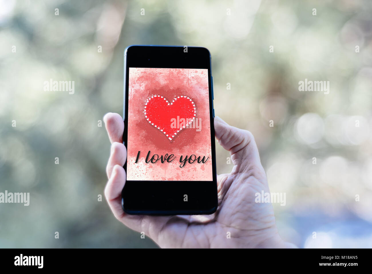 Valentines day sale background with woman hand holding smartphone with heart illustration with the words I Love You on screen mockup against nature ba Stock Photo