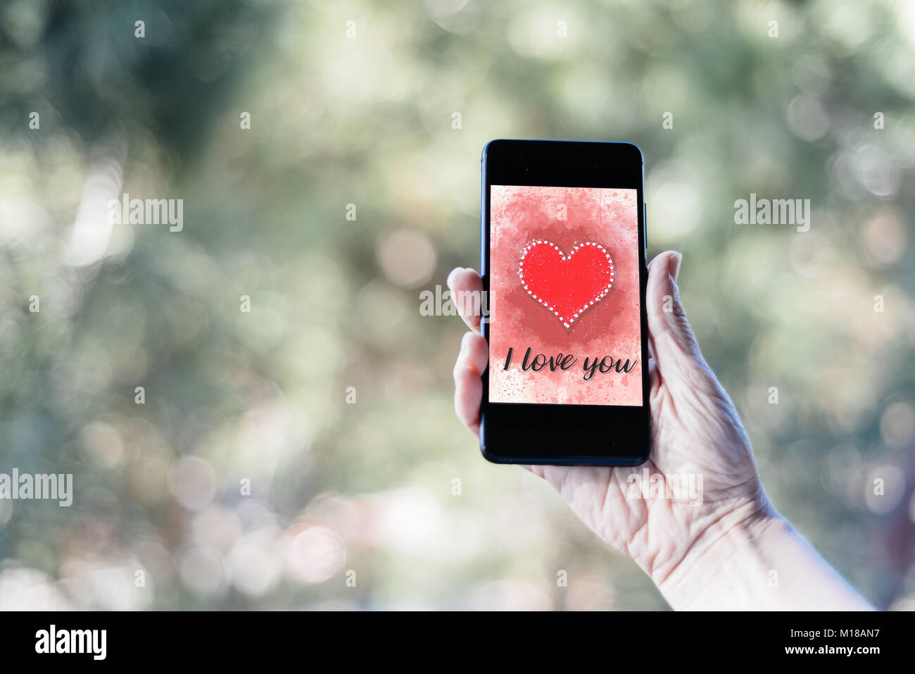 Valentines day sale background with woman hand holding smartphone with heart illustration with the words I Love You on screen mockup against nature ba Stock Photo