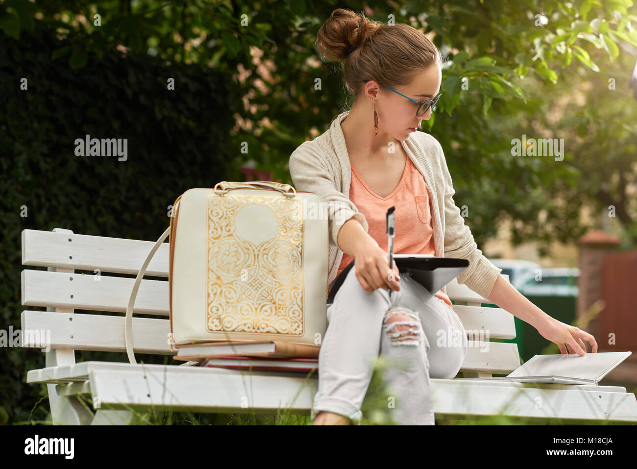 Pretty student studies on a white bech in a city park Stock Photo