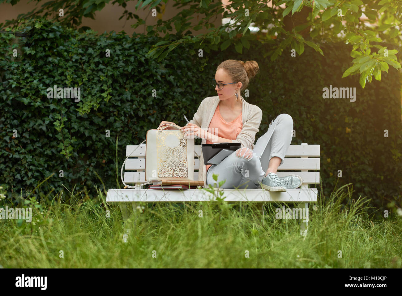 A young girl sits on the white bench in the park Stock Photo