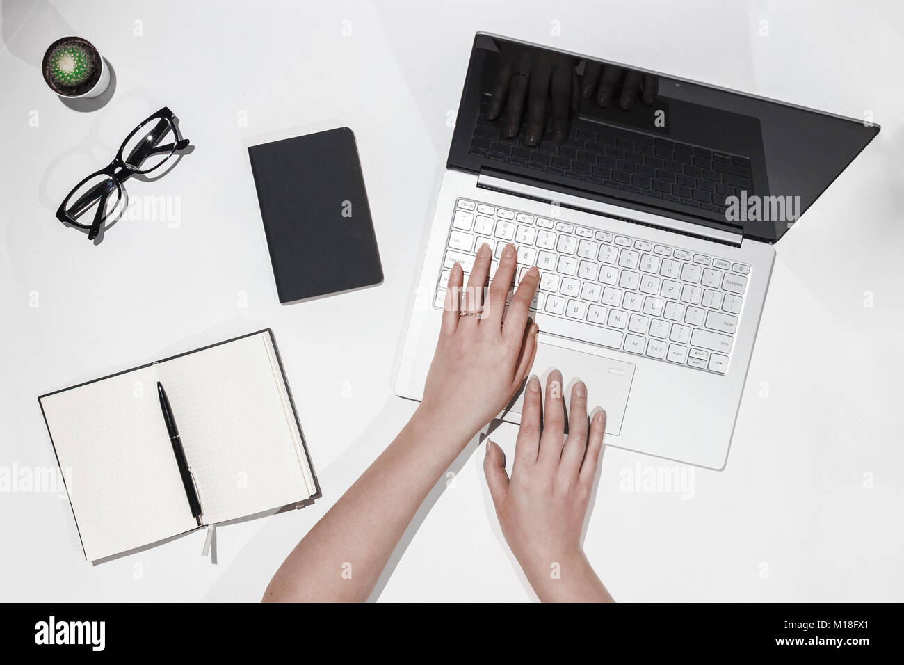 Female hands printing text on laptop. Top view of modern workspace with laptop, cactus, eyeglasses, notebook and pen. Working desk table concept. Stock Photo