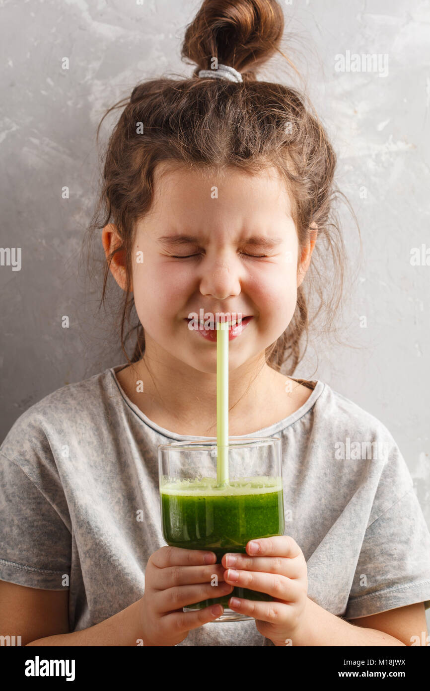 Beautiful happy baby girl drinks healthy green vegetablefruit smoothie