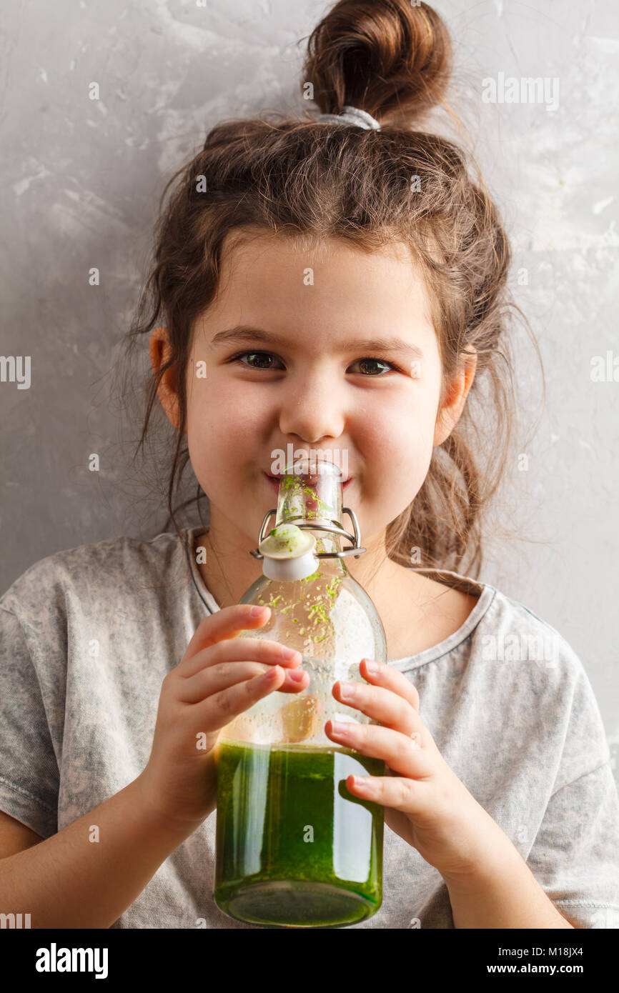 Beautiful happy baby girl drinks healthy green vegetablefruit smoothie