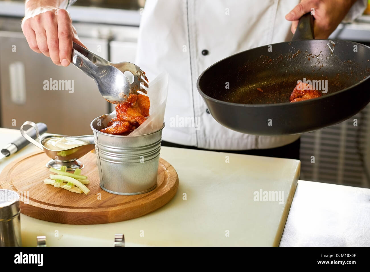 Hot chicken wing bucket filling using kitchen utensil tongs. Stock Photo