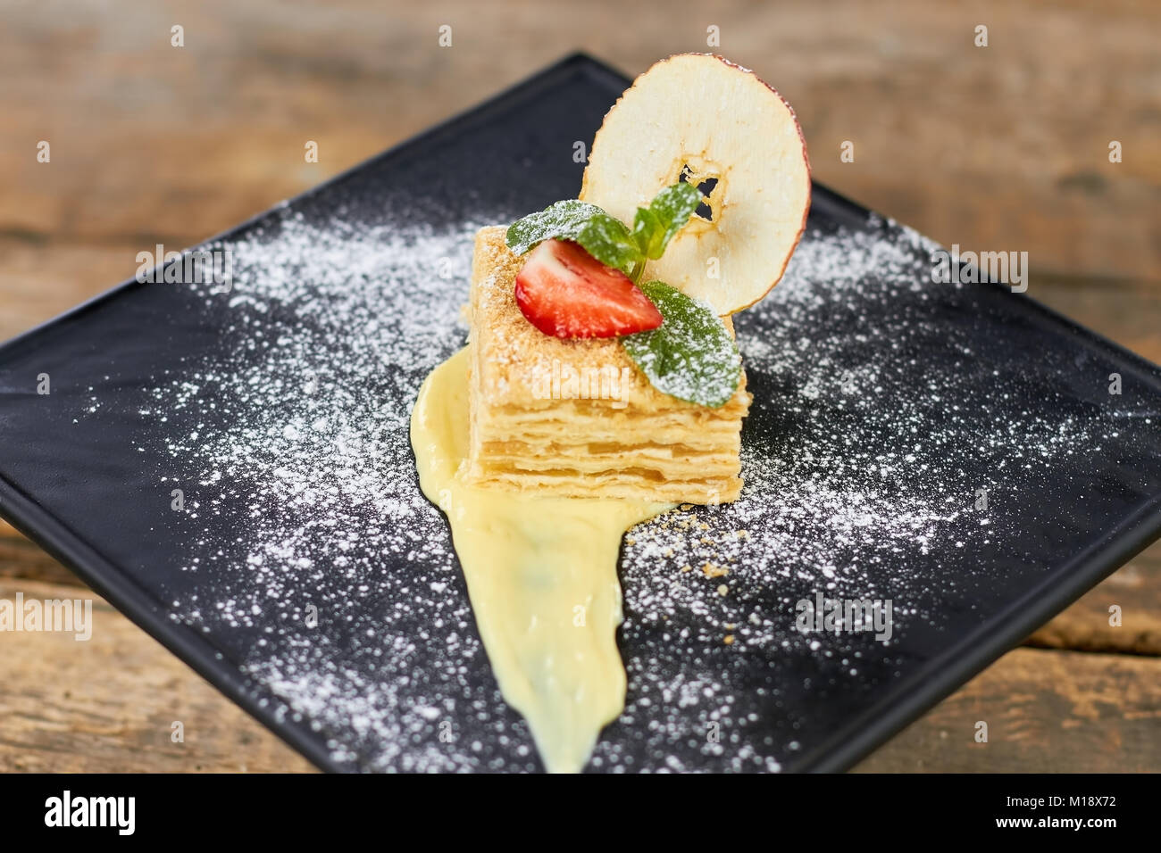 Cake Napoleon of puff pastry with sour cream on a black plate. Stock Photo