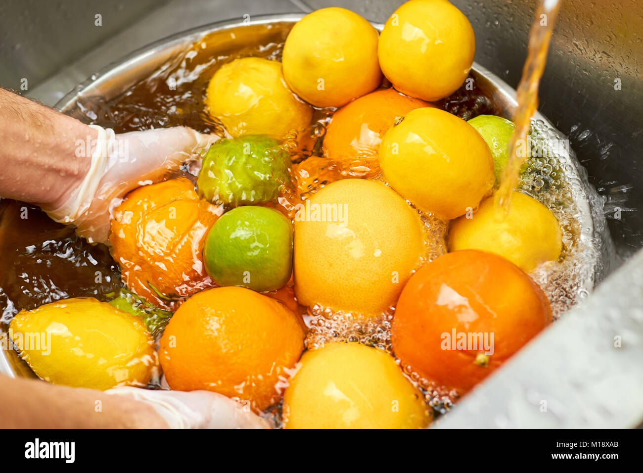 Plenty of citrus fruits in a metal bowl full of water under tap water. Stock Photo