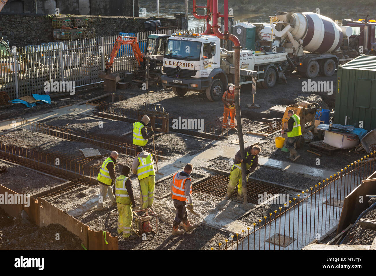 Workmen  in high visibility flourescent jackets on building, pouring concrete into foundations Stock Photo