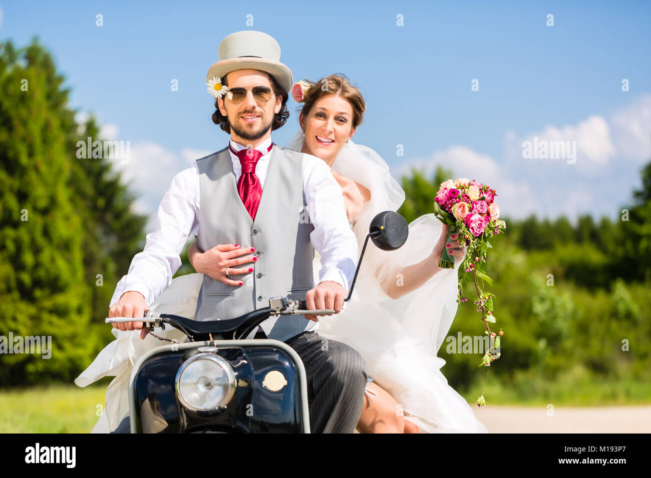 Bridal pair driving motor scooter wearing gown and suit Stock Photo