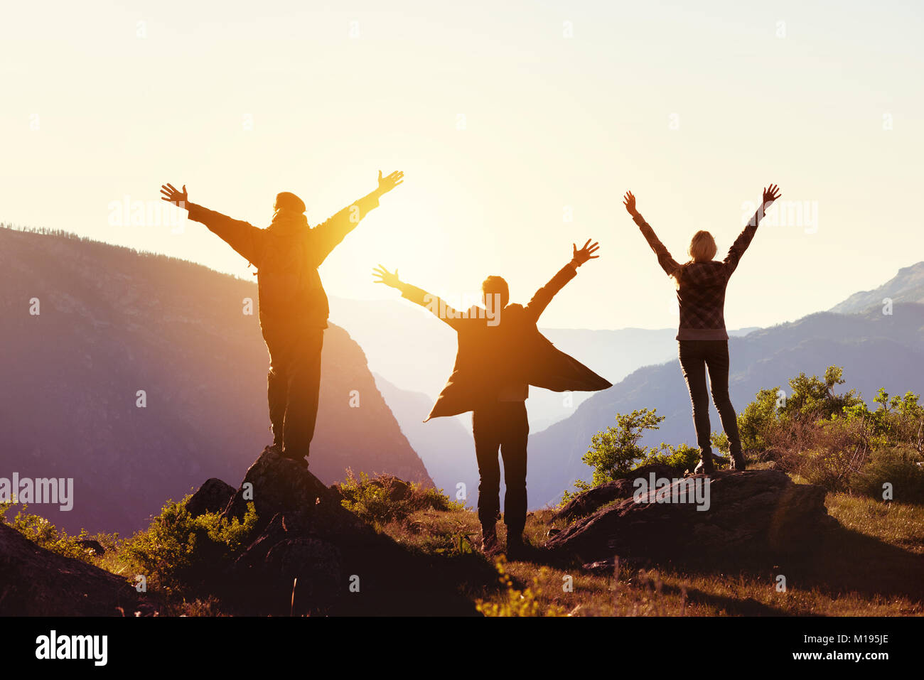 Travel concept with three happy friends against sunset mountains Stock Photo