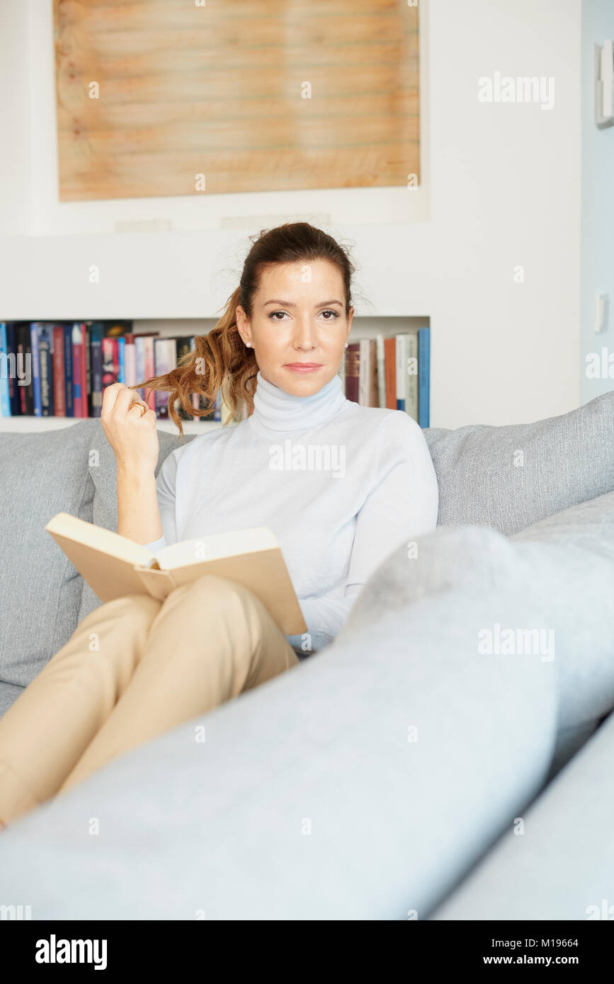 A Beautiful Smiling Mature Woman Reading Book While Sitting On Sofa At