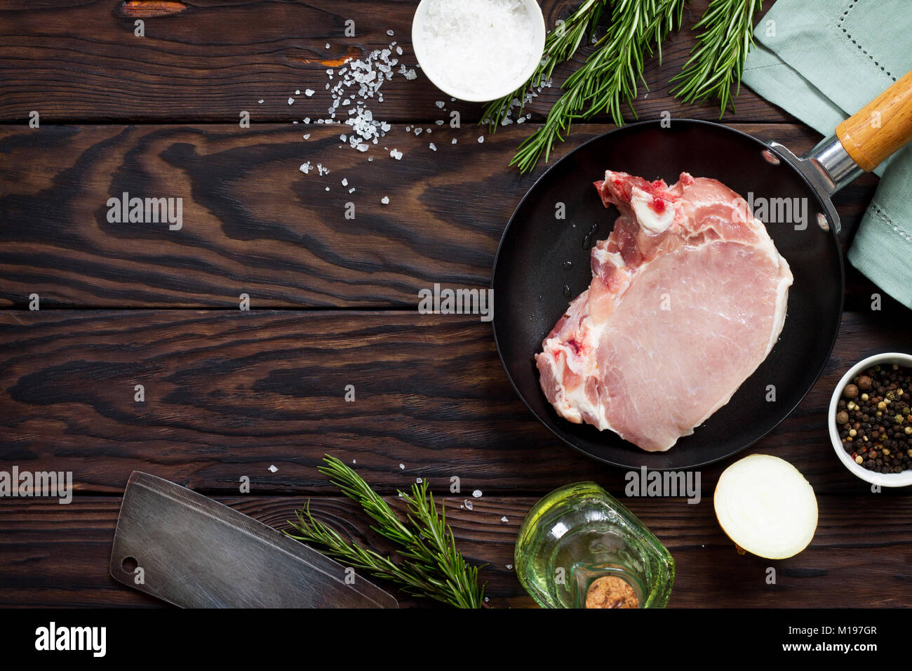 Fresh meat. Raw steak cutlet on a bone on a cast-iron frying pan, olive oil, spices and fresh rosemary on the kitchen table. Stock Photo