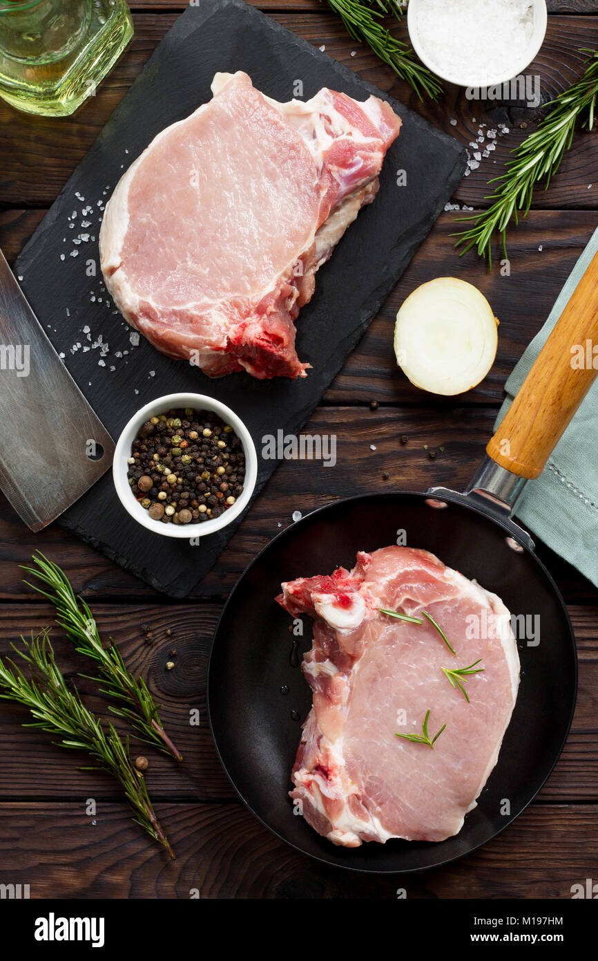 Fresh meat. Raw steak cutlet on a bone on a cast-iron frying pan, olive oil, spices and fresh rosemary on the kitchen table. Stock Photo