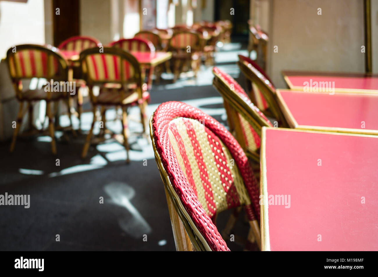 Typical tables and rattan chairs on the terrace of a parisian outdoor cafe in the sunlight. Stock Photo