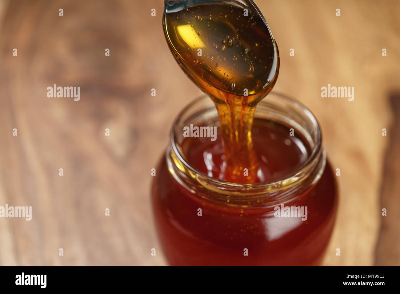 organic honey drips from spoon in jar Stock Photo