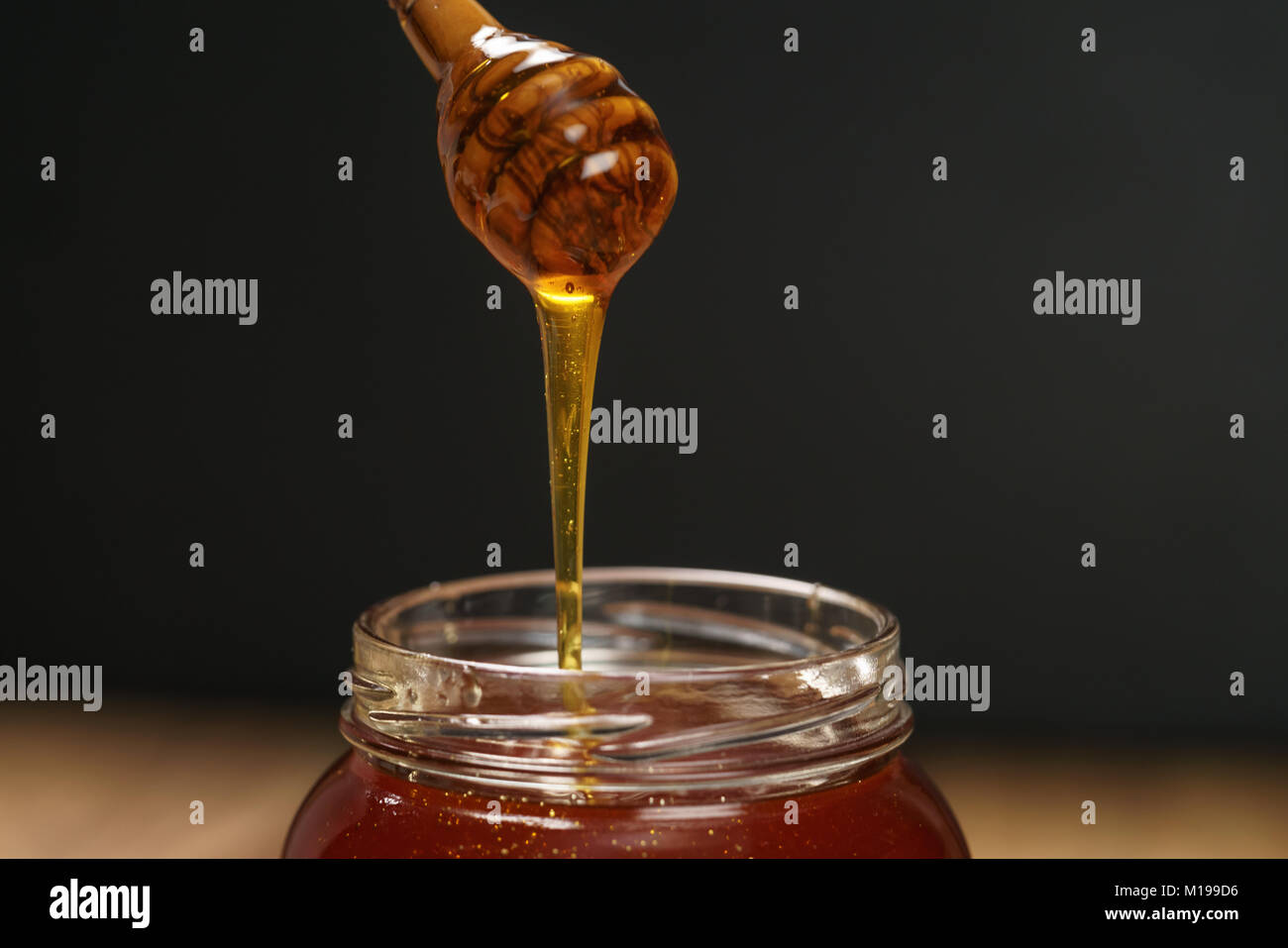 organic honey drips from wooden dipper in jar Stock Photo