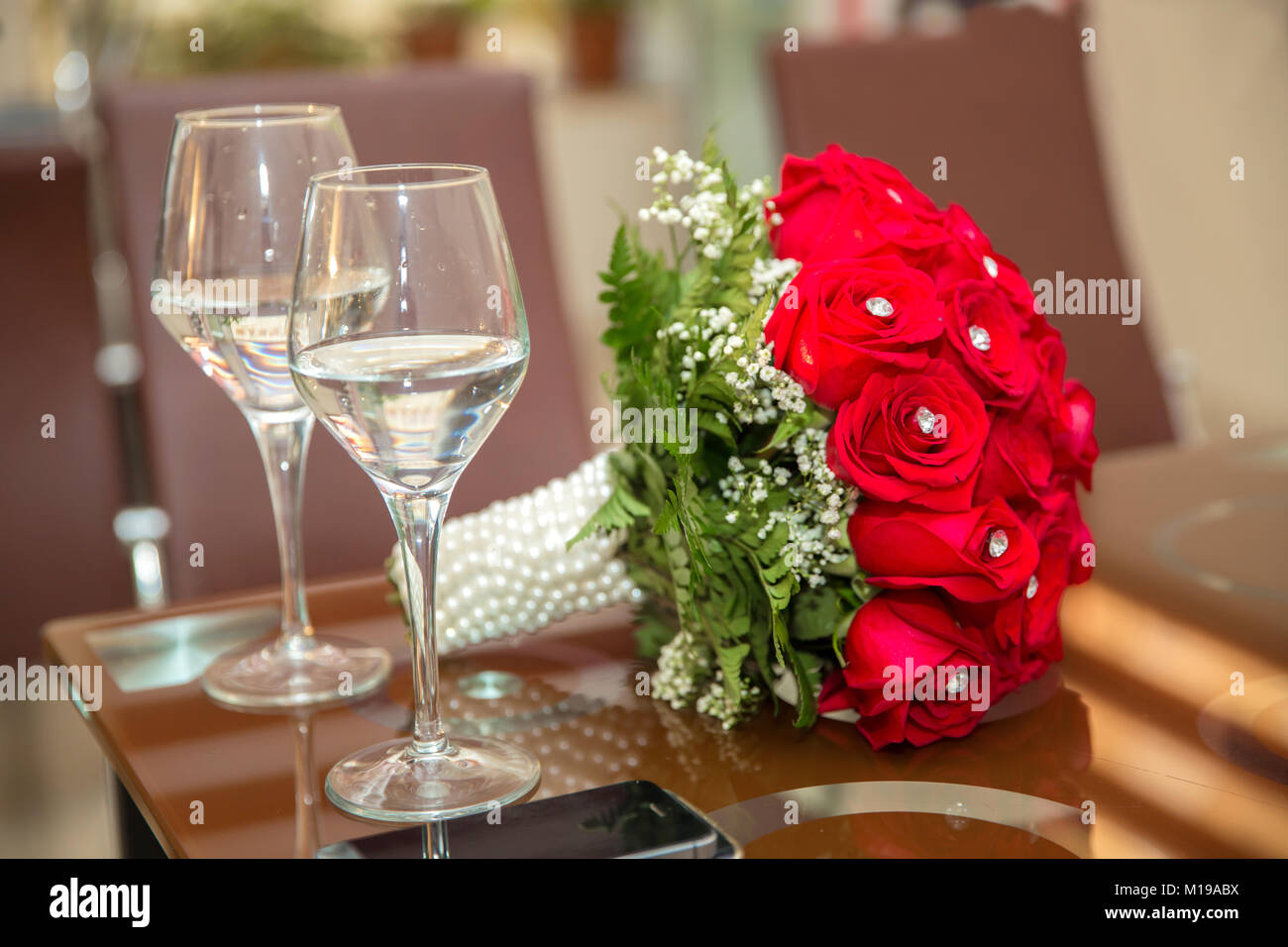 Wedding bouquet of red roses and two champagne glasses standing on the ...