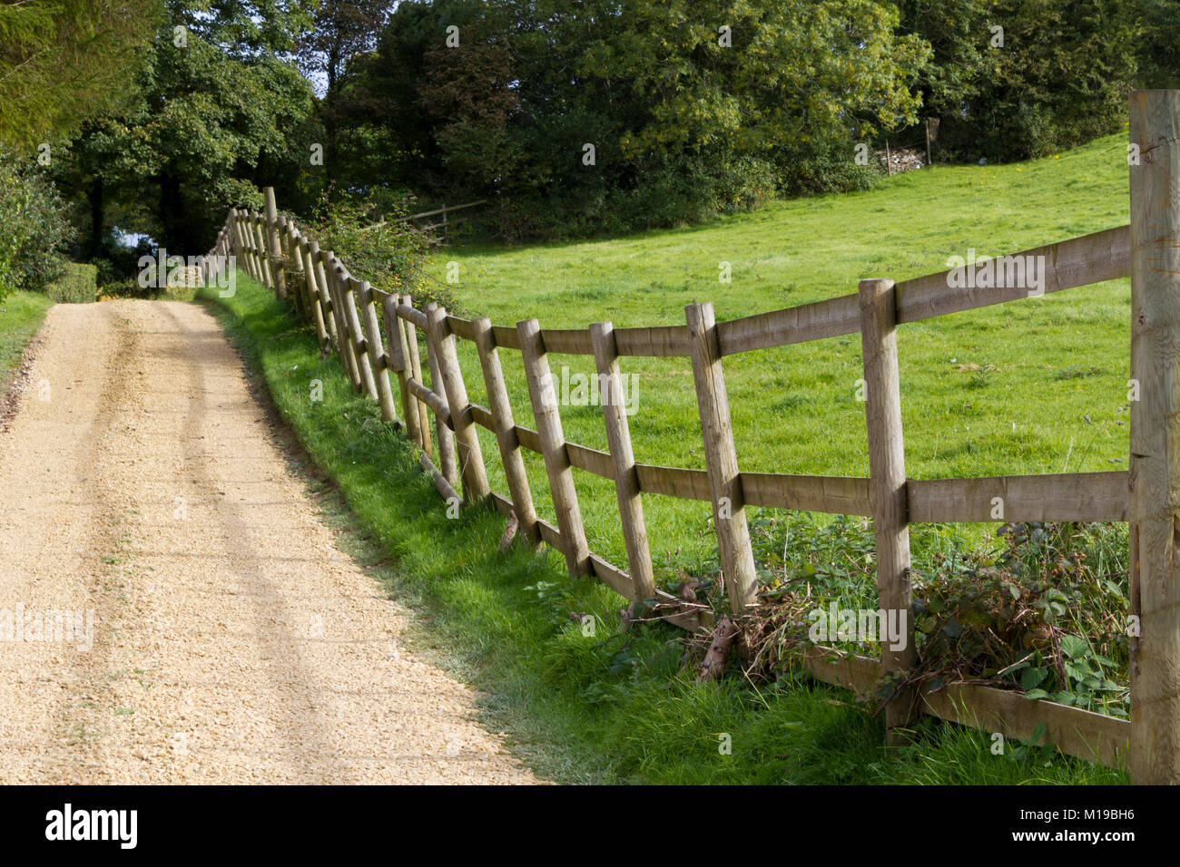 A rustic post and rail fence leans alongside a gravel drive Stock Photo