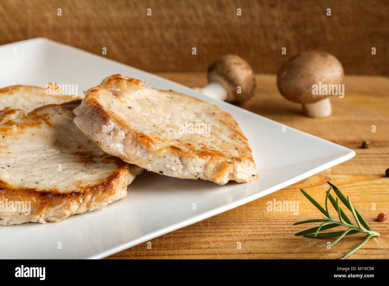 Three pieces of pork sirloin on white plate with wooden background Stock Photo