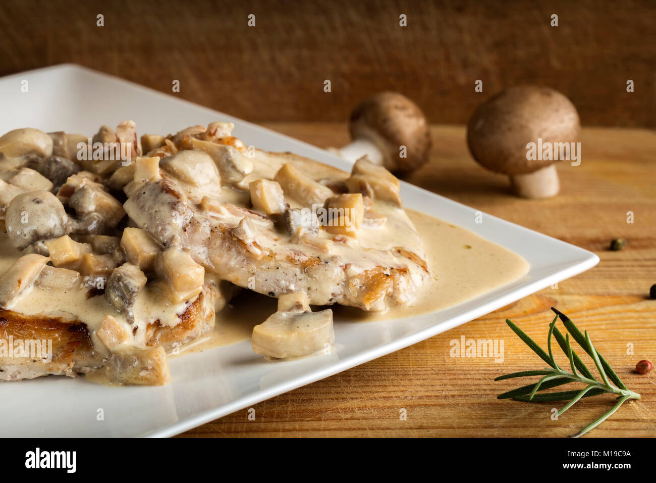 Pork sirloin with white sauce made from sour cream and mushrooms on wooden background Stock Photo