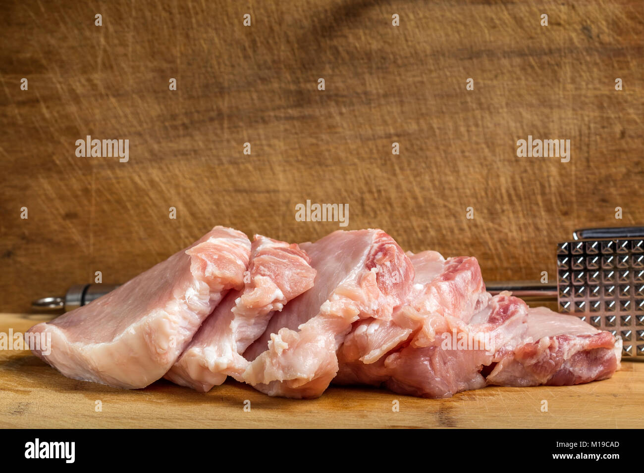 Slices of fresh pork sirloin meat with a metallic hammer for beating meat on wooden cutting board Stock Photo